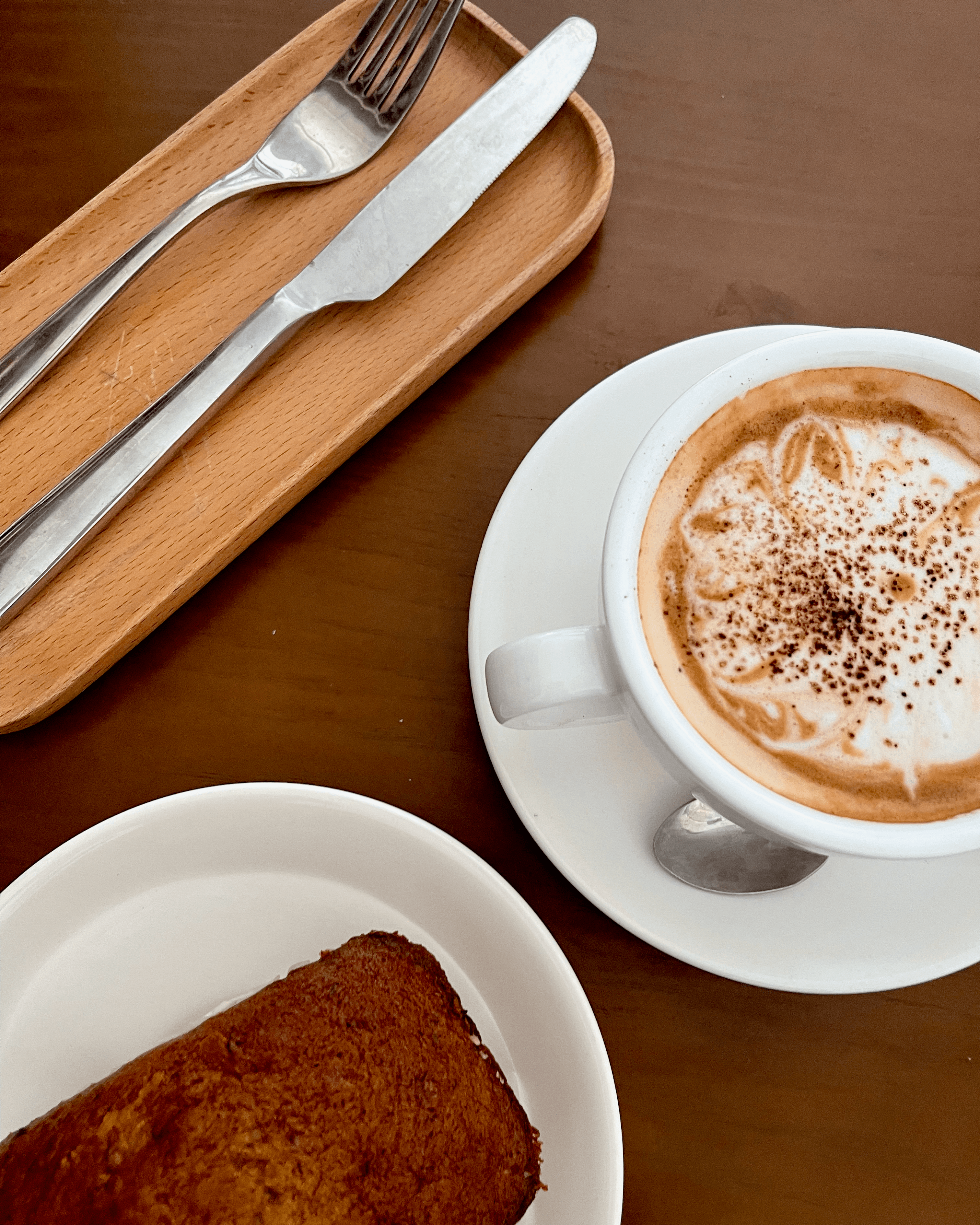 Silverware, banana bread, and cappuccino on a wooden table in Cat Ba, Vietnam