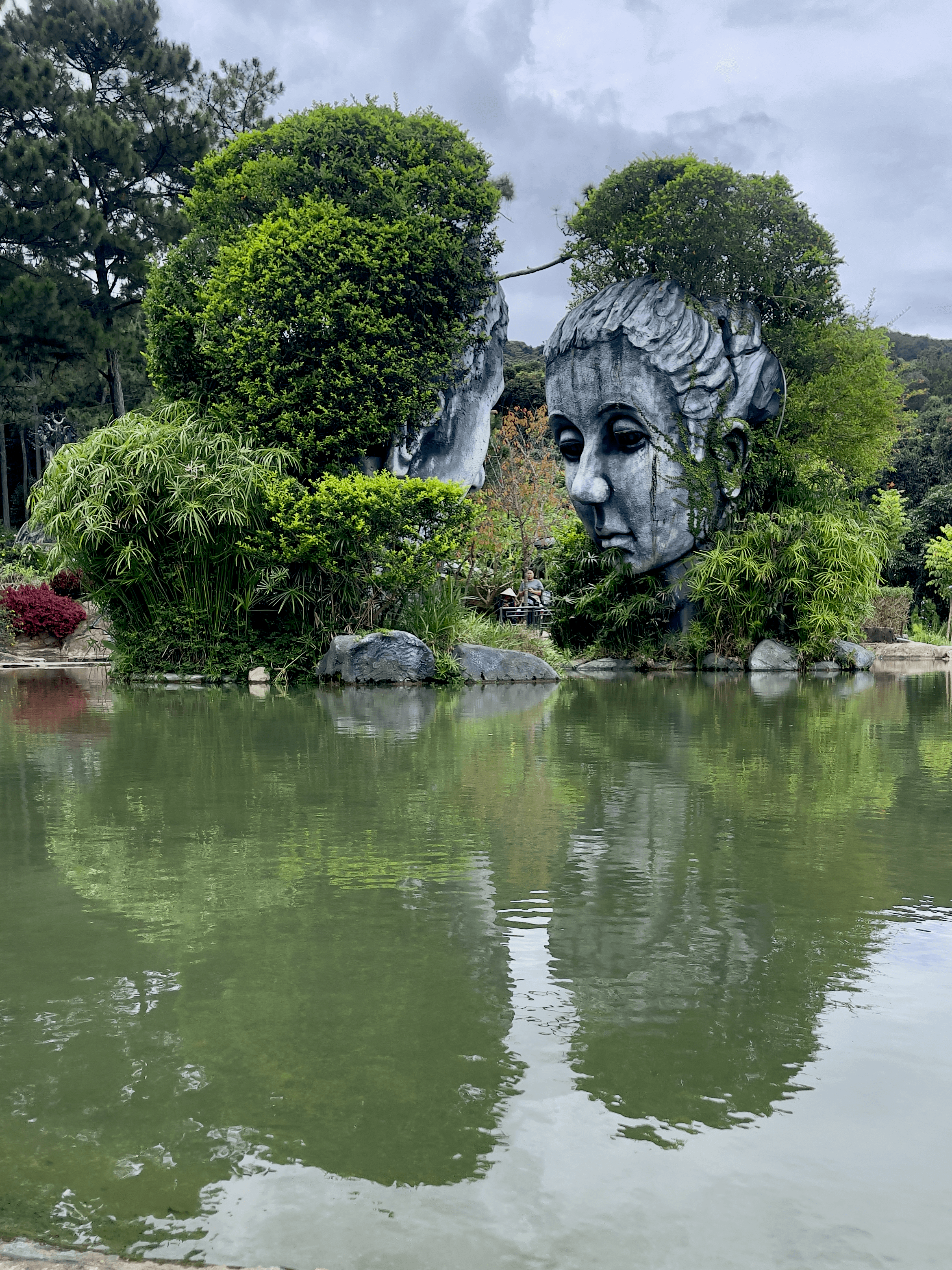 Two large stone face scultures covered in greenery at the Sculpture Tunnel