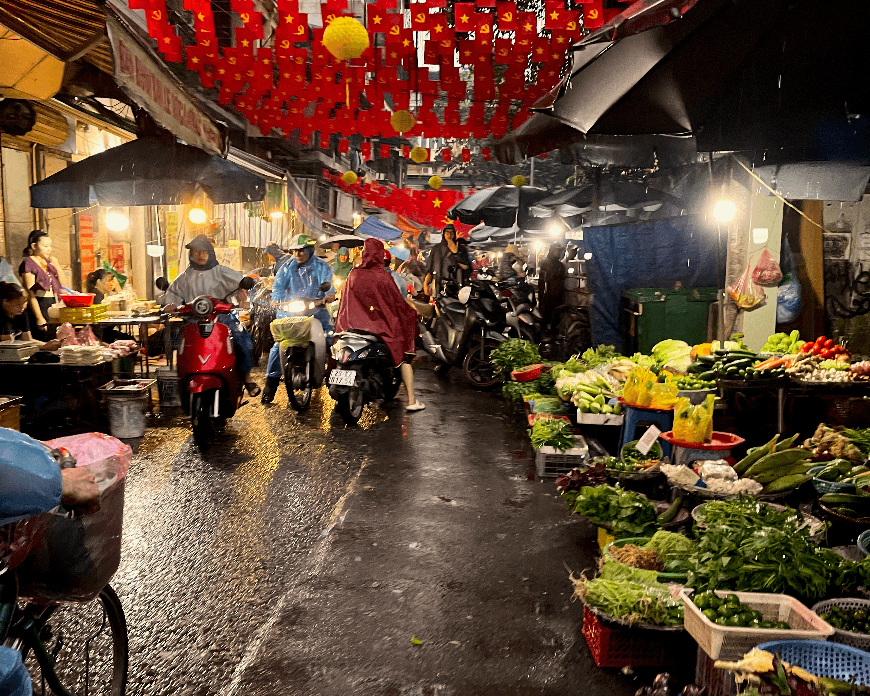 Rainy scene of vegetables, motorbikes, and Vietnam flags in Hanoi