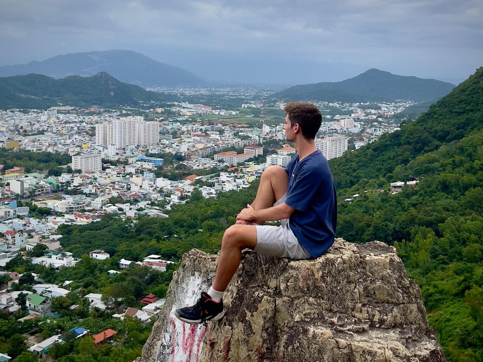 Matthew Fisher sitting on a rock overlooking Nha Trang, Vietnam with mountains